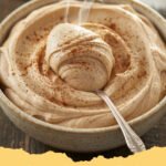 A close-up of a bowl of fluffy cinnamon buttercream frosting with a swirl pattern