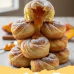 A close-up of golden brown peach pie cruffins coated in cinnamon sugar with a visible peach filling.