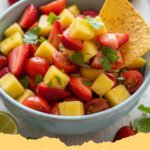 A close up shot of vibrant strawberry pineapple salsa in a glass bowl with tortilla chips.