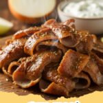 Thinly sliced homemade gyro meat in a pita with tzatziki, tomatoes, and red onion.