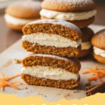 A stack of homemade carrot cake whoopie pies filled with cream cheese frosting, garnished with finely grated carrot.