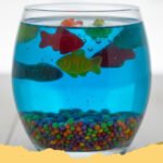 Edible Aquarium Jello Cups Recipe - Close-up of an Edible Aquarium Jello Cup filled with blue Jell-O, graham cracker 'sand', and colorful gummy sharks and fish.