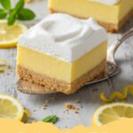 Close-up of Easy Lemon Cream Pie Bars dusted with powdered sugar, on a white serving plate, with a few fresh lemon slices nearby.