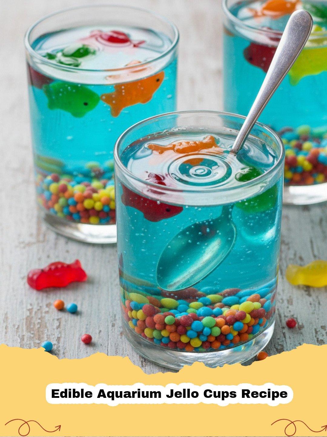 Edible Aquarium Jello Cups Recipe - Close-up of a vibrant Edible Aquarium Jello Cup with gummy fish swimming in blue jello, garnished with a sandy bottom and green seaweed.