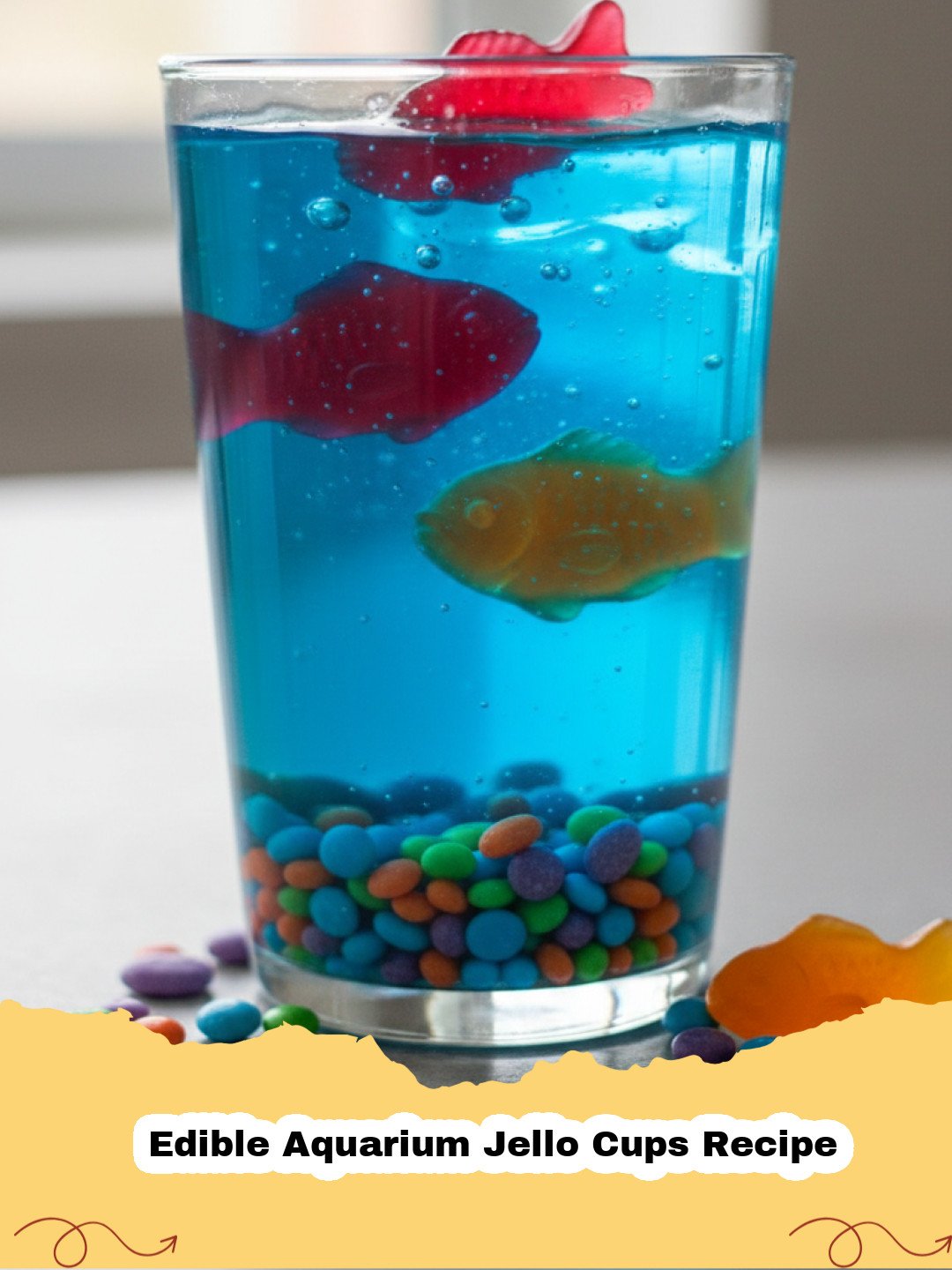 Edible Aquarium Jello Cups Recipe - Close-up of vibrant blue Edible Aquarium Jello Cups filled with candy fish and crushed graham cracker 'sand', ready to be served at a party.