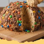 A perfectly coated Reese Peanut Butter No Bake Dessert Cheese Ball on a platter with various dippers like pretzels and graham crackers.