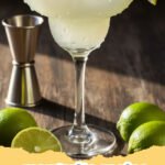 margarita recipe - Two classic margaritas with salted rims and lime garnishes, sitting on a wooden table, with a blurred background of a sunny patio.