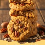 Close-up of a stack of Pecan Pie Oatmeal Cookies on a cooling rack with loose pecans and oats around.