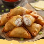 crab rangoons recipe - Pile of crispy golden homemade crab rangoons on a white plate with a small bowl of sweet and sour sauce.