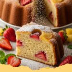 A beautifully glazed Strawberry Pineapple Pound Cake on a white cake stand, garnished with fresh strawberries and mint leaves, with slices visible.