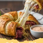 Golden brown Reuben Crescent Bake in a baking dish, sliced into squares, with melted cheese and corned beef visible