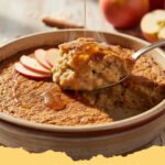 Close-up of a warm oatmeal apple breakfast bake in a baking dish, with a scoop removed.