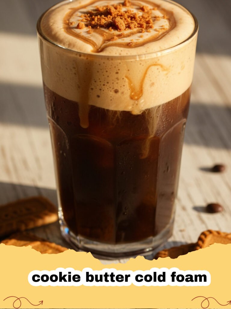 Close-up of a glass of iced coffee topped with a thick layer of cookie butter cold foam, garnished with crushed Biscoff cookies.