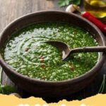 chimichurri recipe - A vibrant green bowl of classic Argentinian chimichurri sauce with fresh herbs in the background.
