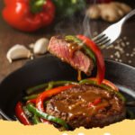 pepper steak recipe - A steaming skillet of classic pepper steak with tender beef, colorful bell peppers, and a rich, glossy sauce, garnished with green onions and sesame seeds, served over white rice.