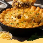 cowboy casserole recipe - A golden brown cowboy casserole with crispy tater tots and melted cheese in a glass baking dish.