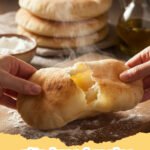 pita bread recipe - Stack of warm, freshly baked homemade pita bread, perfectly puffed and golden brown, on a wooden board next to a bowl of hummus.