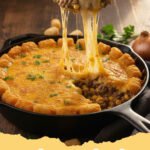 cowboy casserole recipe - A close-up of a bubbling, cheesy cowboy casserole topped with crispy golden tater tots, fresh green onions, and a dollop of sour cream.