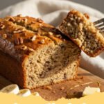 banana nut bread recipe - A golden brown loaf of banana nut bread sliced on a wooden board.