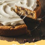 cookie cake recipe - A large decorated chocolate chip cookie cake with buttercream frosting on a wooden board.