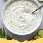 ranch dressing recipe - A glass jar filled with creamy white ranch dressing surrounded by fresh herbs and carrot sticks.