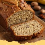 banana nut bread recipe - A golden brown loaf of banana nut bread sliced on a wooden board.