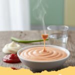 yum yum sauce recipe - Creamy homemade yum yum sauce in a small white bowl, garnished with a sprinkle of paprika, beside a plate of grilled chicken and rice.