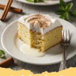 tres leches cake recipe - A slice of incredibly moist tres leches cake topped with fresh whipped cream and a sprinkle of cinnamon, served on a white plate.