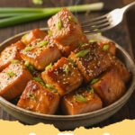 salmon bites recipe - Close-up of golden brown, perfectly seared salmon bites garnished with fresh parsley and lemon wedges on a white plate.