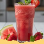 watermelon smoothie recipe - A tall glass of pink watermelon smoothie with a mint garnish and lime wedge on a sunny table.