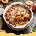 easy peach cobbler recipe - A golden brown peach cobbler in a glass baking dish with a scoop of vanilla ice cream.