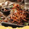 pulled pork recipe - Close-up of perfectly shredded slow-cooked pulled pork on a wooden cutting board, ready to be served.