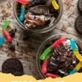 Close-up of individual Dirt Cake Dessert Cups with gummy worms peeking out from chocolate cookie crumbs.