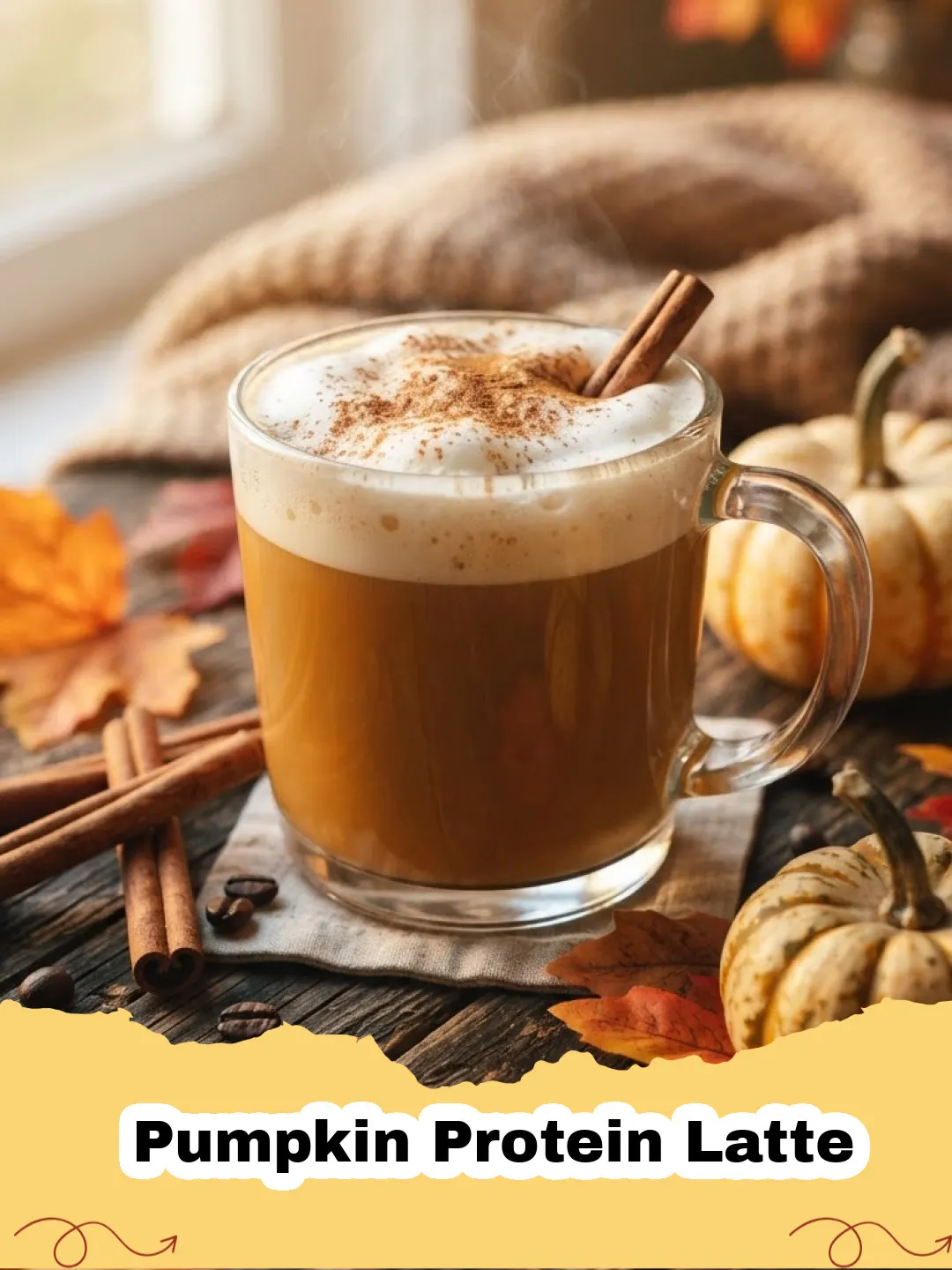 A cozy mug of frothy Pumpkin Protein Latte topped with whipped cream and a sprinkle of cinnamon on a wooden surface with autumn leaves.