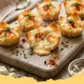 Golden brown Creamy Harissa & Cheese Phyllo Bites stacked on a white plate, garnished with fresh parsley and a side of dipping sauce.