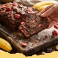 A moist loaf of Chocolate Banana Strawberry Bread on a cooling rack, sliced to reveal bananas, strawberries, and chocolate chips.