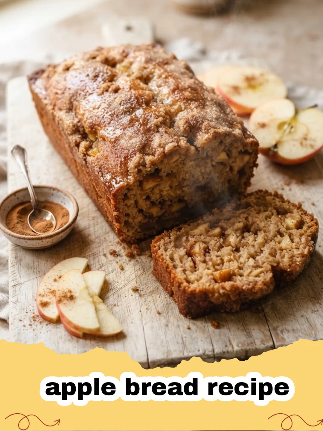 apple bread recipe - A moist slice of spiced apple bread with whole apples and cinnamon sticks in the background.