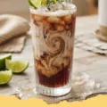 A close-up of a refreshing Diet Coke Coconut Lime Dirty Soda in a tall glass with ice and a lime wedge.