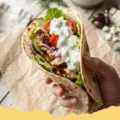 Greek Yogurt Tzatziki Chicken Wraps - Close-up of a freshly made Greek Yogurt Tzatziki Chicken Wrap, filled with grilled chicken, creamy tzatziki, fresh lettuce, and tomatoes, neatly folded and ready to eat.