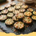 roasted zucchini recipes - Close-up of perfectly roasted zucchini pieces with garlic and herbs on a baking sheet, with golden-brown edges.