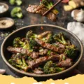 broccoli beef recipe - A close-up of a serving of homemade broccoli beef stir-fry with tender slices of beef, bright green broccoli, and a glossy brown sauce, served over white rice.