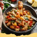 sweet and sour chicken recipe - Close-up of crispy sweet and sour chicken with colorful bell peppers and pineapple chunks, garnished with sesame seeds, served with rice.