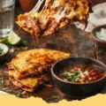 Masienda Beef Birria Quesadillas - Crispy Masienda Beef Birria Quesadilla with melted cheese and tender beef, garnished with cilantro and onion, with a side of rich consommé for dipping.