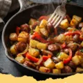 Close-up of a sheet pan filled with roasted Italian sausage and potato recipes, golden brown and garnished with fresh rosemary.