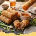 Crispy Rice Paper Egg Rolls - Pile of golden crispy rice paper egg rolls with fresh herbs and a dipping sauce.