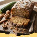 zuchinis bread recipe - Two golden-brown loaves of moist zucchini bread on a cooling rack, with one slice cut out.