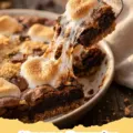 Close-up of a pan of freshly baked S'mores Brownies, with gooey toasted marshmallows, rich chocolate brownie, and a visible graham cracker crust.