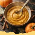 Slice of moist spiced pumpkin bread on a wooden board with a cup of coffee and autumn leaves, representing cozy pumpkin puree recipes.